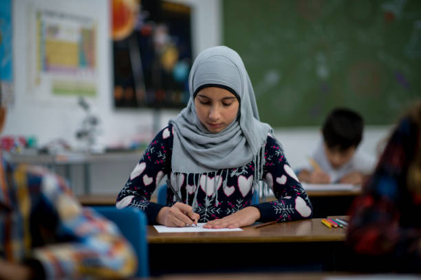 Muslim girl doing a school assignment in a classroom A young Muslim student in elementary school is working on a writing or math assignment in the classroom.  She is wearing a hijab. womens issues stock pictures, royalty-free photos & images