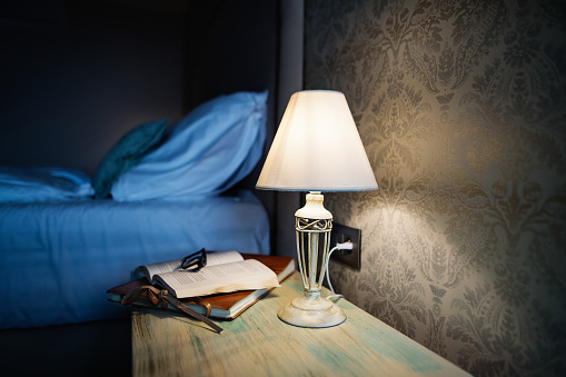 Hotel room in the evening. Bedside lamp lit on the bedside table next to the bed in a hotel room.