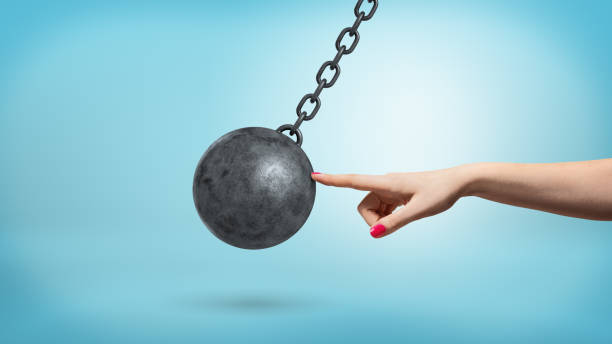 um braço feminino gigante com um dedo tocar levemente um ferro preto bola de demolição e parar o seu movimento. - wrecking ball destruction chain sphere - fotografias e filmes do acervo