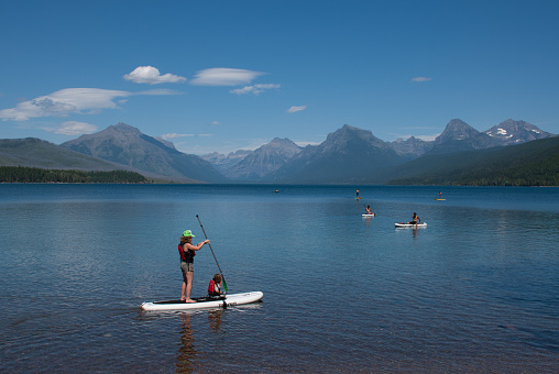 Paddleboarders and boaters enjoy a sunny day and calm water on Lake McDonald in Glacier National Park in July 2017. Glacier National Park is in northwest Montana, USA.