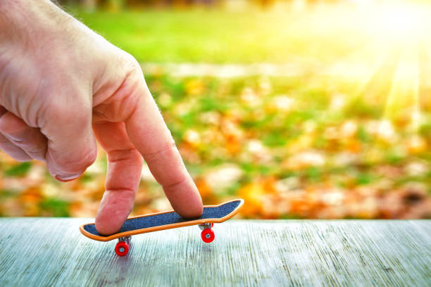 Fingers of hand skate on toy skateboard against green sunny background. concept of youth stock photo
