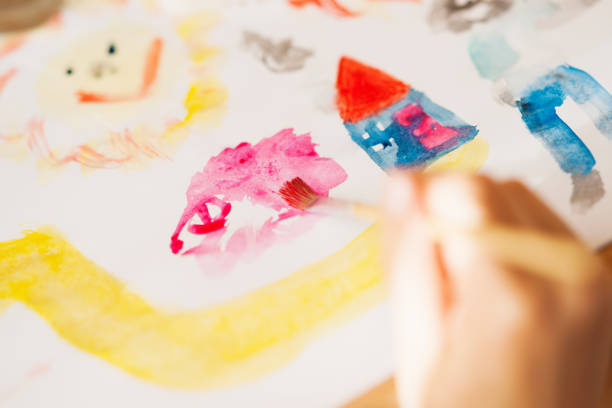istock Hand with paintbrush draw house,sun and people 869102730