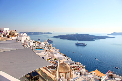 A view in Santorini, Greece with beautiful views of the whitewashed buildings, cliffs and sea. The famous caldera island is in the background along with several cruise ships.