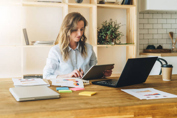 istock Young businesswoman woman is sitting at kitchen table and uses tablet computer, working, studying. 869122602