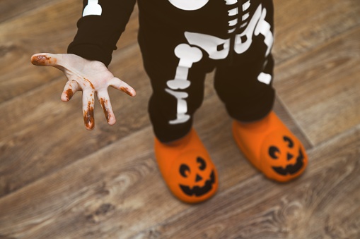 Hand is stained with chocolate. There is pumpkin slippers on his feet.