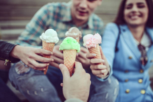 Smiling Friends Eating Ice Cream and Holding Cones in Hands Smiling Teenage Friends Eating Ice Cream and Holding Cones in Hands licking ice cream cone stock pictures, royalty-free photos & images
