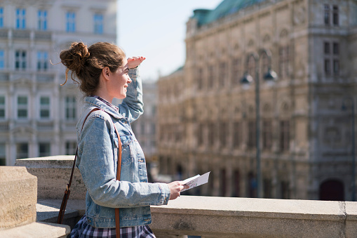 Young female tourist standing on the balcony and looking at the old town of Vienna.