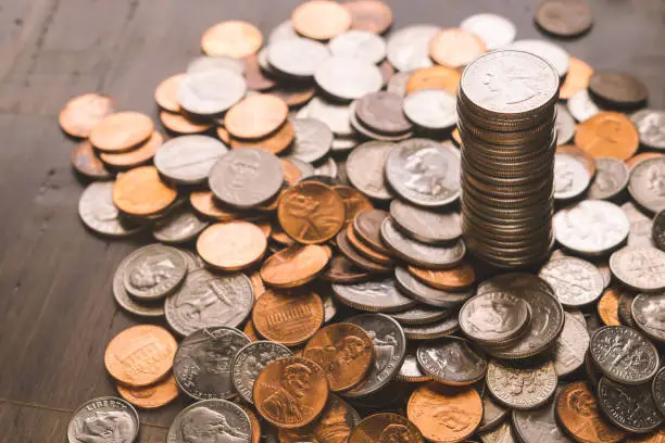 Tower of quarters with money spread of bamboo wood background and includes quarters, nickels, dimes, and pennies.