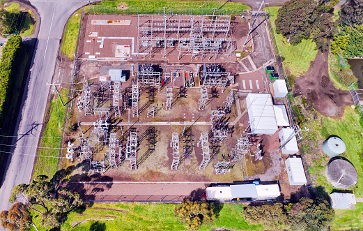 Distributing high voltage power substation in regional Australian town viewed from above on a block of land made of insulators, poles, wires and transformers.