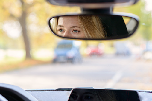 Eyes of a female driver reflected in the rear view mirror inside a car with a view through the blurred windscreen and copy space