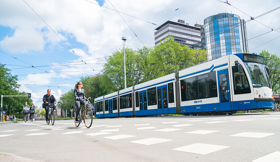 People cycle with tram through city intersection with modern office buildings in background low point of view