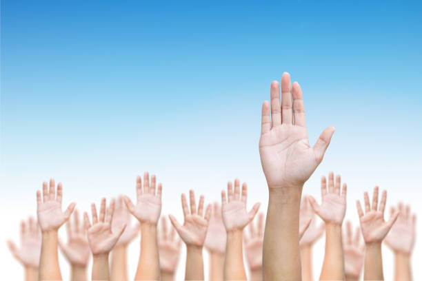 Business crowd raising hands high up on blue skies background. stock photo