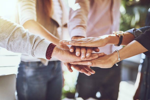 Shot of a group of colleagues joining hands in solidarity outdoors