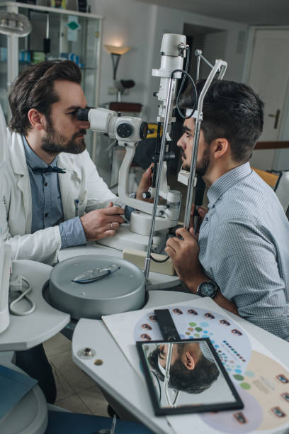 istock Male ophthalmologist examining young man's eyesight with optical instrument. 869234580