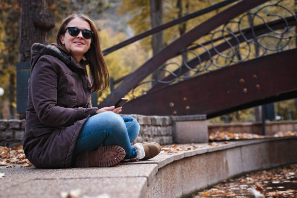romantic girl sitting on a bench in the city with her arms around her knees and with a young man in background