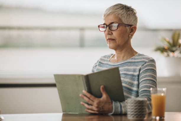 istock Pensive senior woman reading a book at home. 869246586