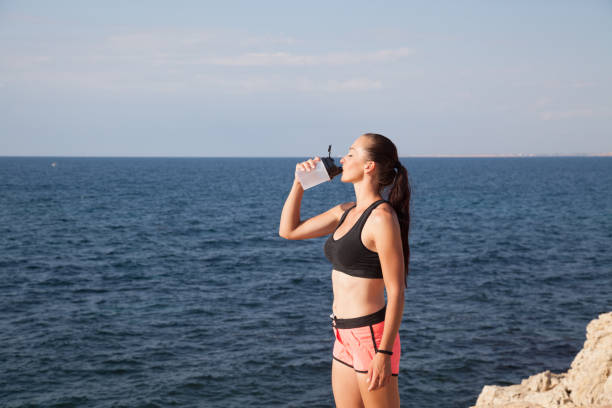 istock girl drinking water from a shaker after a workout on the beach 869253898
