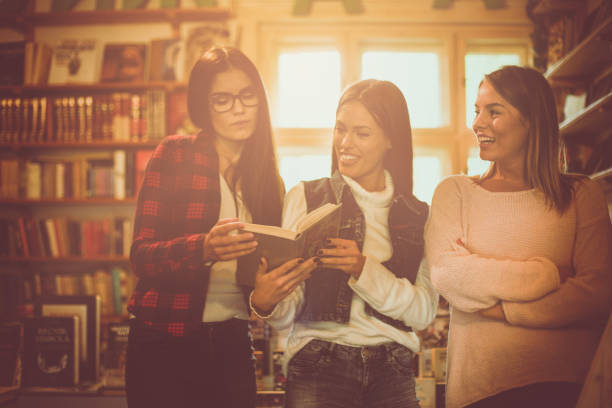 Three young students girls in library reading book together  and having conversation. Three young students girls in library reading book together and having conversation. dealing room photos stock pictures, royalty-free photos & images