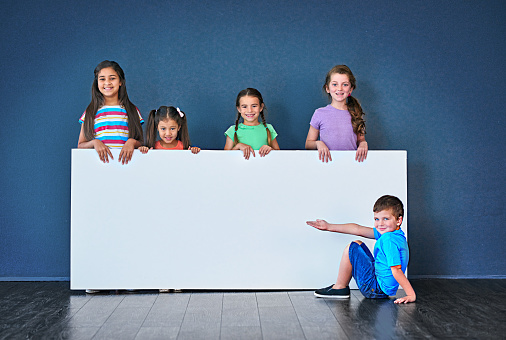 Studio shot of a diverse group of kids standing behind a large blank banner against a blue background