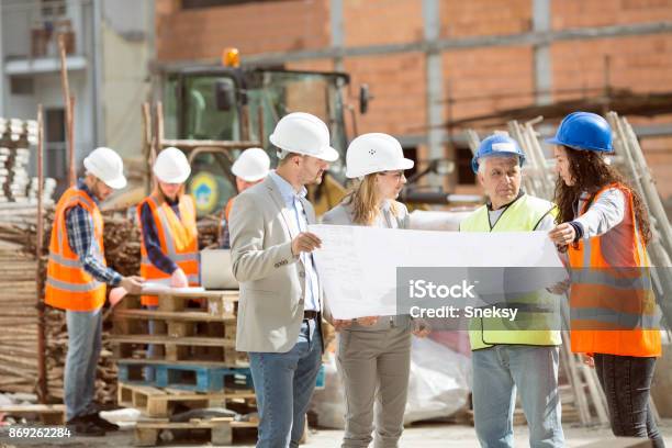 Gruppe Bauarbeiter Blick Auf Blaupausen Auf Baustelle Stockfoto und mehr Bilder von Baustelle