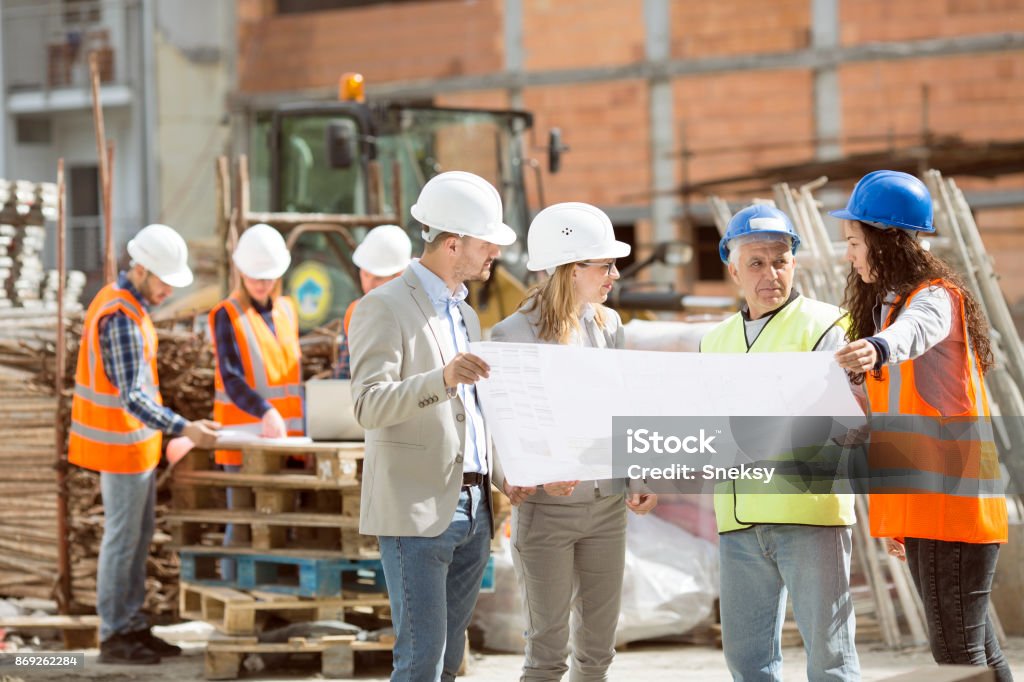 Group Construction workers looking at blueprints on construction site Construction workers talking on site Construction Site Stock Photo