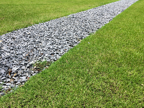 Gray gravel walking path in a grass field/lawn of a garden