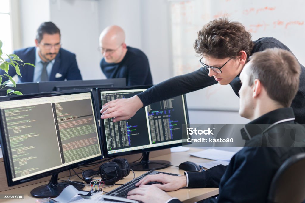 Startup business problem solving. Software developers working on desktop computer. Startup business and entrepreneurship problem solving. Young AI programmers and IT software developers team brainstorming and programming on desktop computer in startup company share office space. Computer Programmer Stock Photo