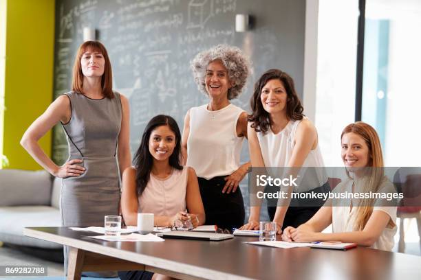 Photo libre de droit de Cinq Collègues Féminines Lors Dune Réunion De Travail Souriant À La Caméra banque d'images et plus d'images libres de droit de Femmes