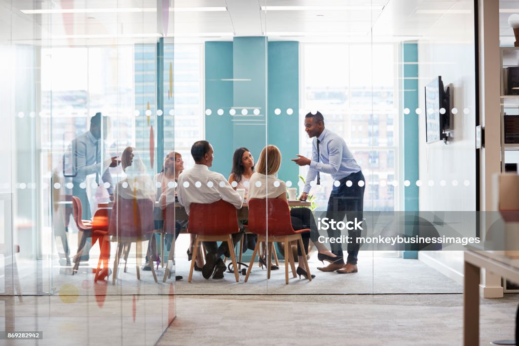 Il giovane capo maschio sta appoggiato sul tavolo durante un incontro di lavoro - Foto stock royalty-free di Riunione commerciale