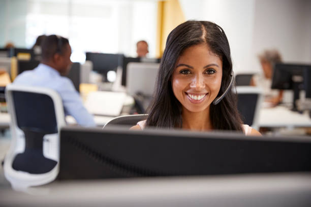 istock Young woman working at computer with headset in busy office 869285968