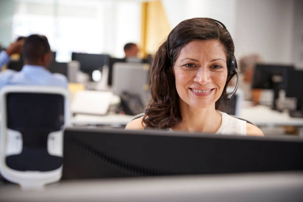 donna di mezza età che lavora al computer con le cuffie in ufficio - solo una donna matura foto e immagini stock