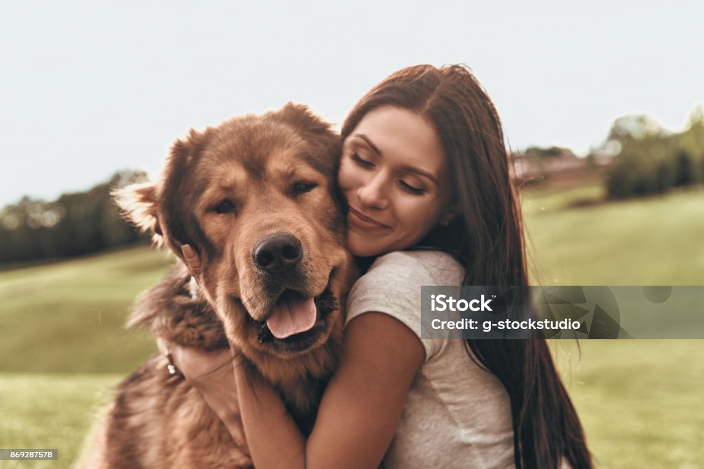 Her best friend. Beautiful young woman keeping eyes closed and smiling while embracing her dog outdoors Dog Stock Photo