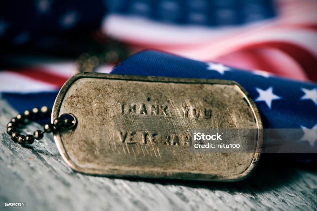 text thank you veterans in a dog tag closeup of a rusty dog tag with the text thank you veterans engraved in it, next to a flag of the United States, on a rustic wooden surface Veteran Stock Photo