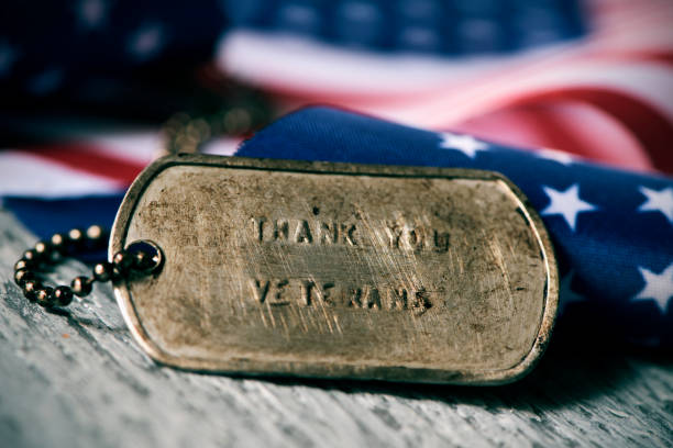 text thank you veterans in a dog tag closeup of a rusty dog tag with the text thank you veterans engraved in it, next to a flag of the United States, on a rustic wooden surface army soldier photos stock pictures, royalty-free photos & images