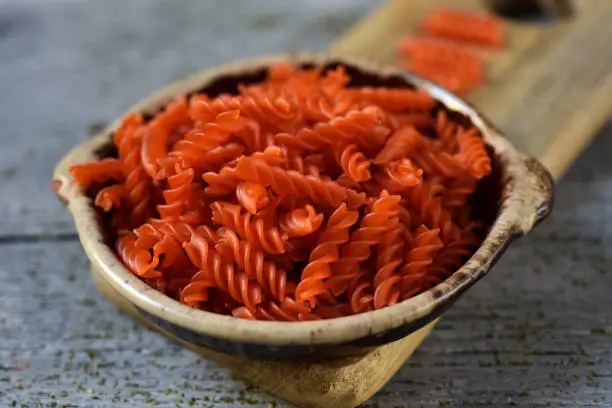 closeup of an earthenware bowl full of uncooked red lentil fusilli on a gray rustic wooden table