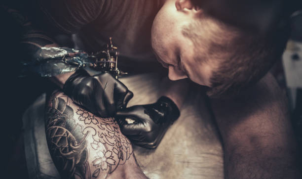 istock Tattoo master making tattoo on customer's leg 869291720