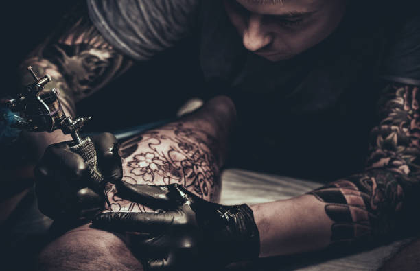 istock Tattoo master making tattoo on customer's leg 869291940