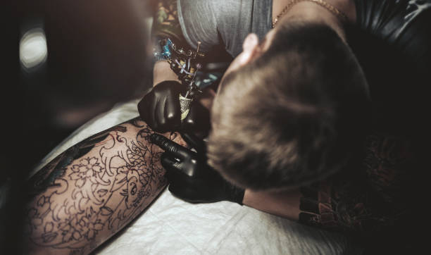 istock Tattoo master making tattoo on customer's leg 869291968