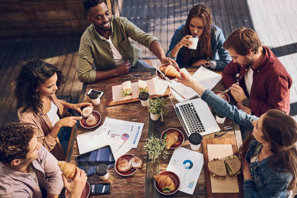 Catching up on statistics while enjoying a good bite Shot of a group of creative workers having a meeting over lunch in a cafe business lunch stock pictures, royalty-free photos & images