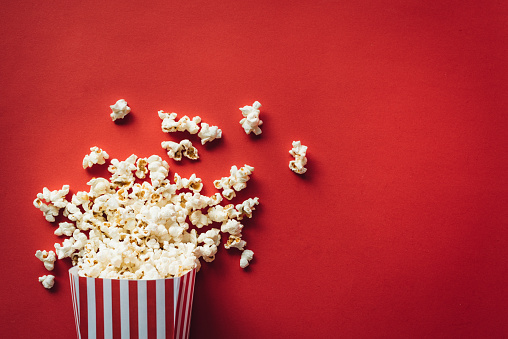 Stock photo showing close-up view of striped carton of popcorn in cinema / movie theatre. Caramelised / caramel toffee popcorn as movie snack food besides 3D glasses in cinema with empty blue seats.