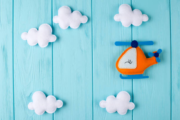 Orange craft helicopter and clouds on blue wooden background with copyspace. Felt handmade toys. Empty space for text. Top view. Orange craft helicopter and clouds on blue wooden background with copyspace. Felt handmade toys. Empty space for text. Top view. Concept for travel agency, business development, card, banner, flyer. felt textile stock pictures, royalty-free photos & images