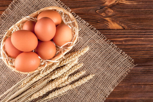 istock Chicken eggs horizontal banner. Eco farming concept. Red eggs and wheat ears on piece of sacking on brown wooden textured background. Organic food. 869303368