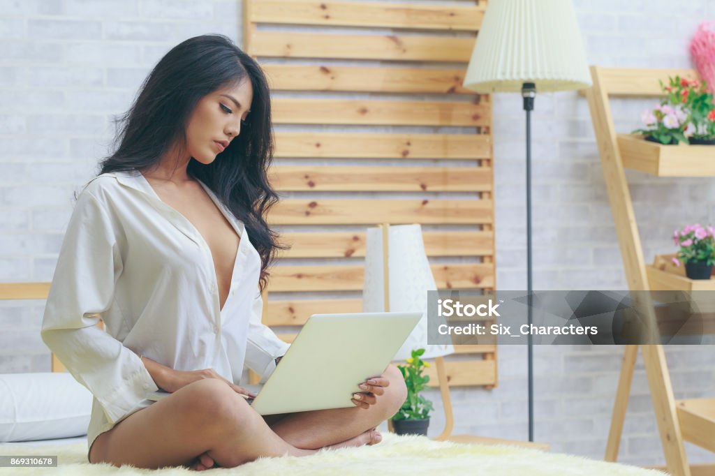 Asian woman in white shirt with laptop in the bedroom Sensuality Stock Photo
