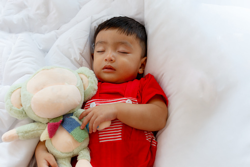 Sleeping Asian baby in his bed and holding a monkey doll