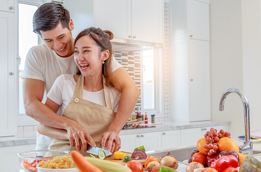 Happy young Asian couple cooking healthy food together in the kitchen at home