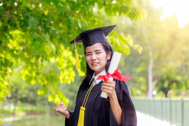 istock Successful graduating student wearing cap and gown holding diploma 869330650