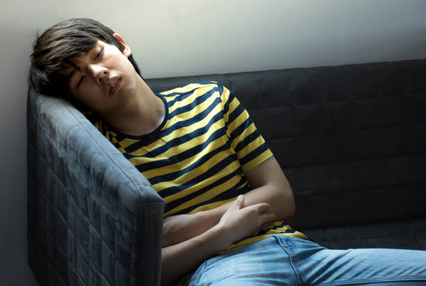 Too much work tired sleepy young man sitting at desk with books in front of laptop computer isolated grey brick wall background. Busy schedule in college, workplace, sleep deprivation concept