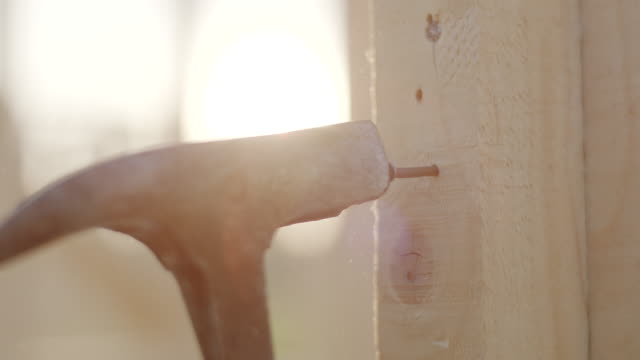 Close up, using hammer to stuck nail in to the wood
