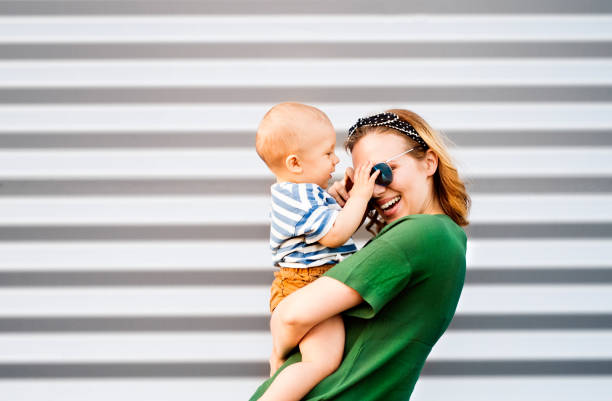 jeune femme avec un petit garçon debout contre le mur. - baby people headband portrait photos et images de collection