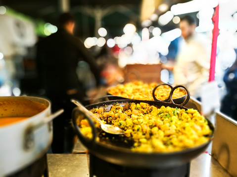 Horizontal color close up image depicting a huge pan of freshly cooked curry at Borough Market, one of the biggest and most popular food markets in London. The dish has a vibrant yellow color and people are blurred out of focus in the background. Lots of room for copy space.